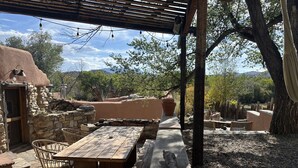 An outdoor patio with stone walls, wooden furniture, and a pergola with string lights. - Skier's Hideaway in Los Cerrillos (Los Cerrillos)