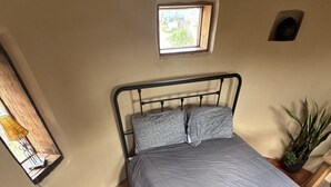 A single bed with a grey quilt, a small window, a potted plant, and a wooden floor. - Skier's Hideaway in Los Cerrillos (Los Cerrillos)