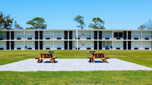 Un motel con una hilera de habitaciones, cada una con puerta y ventana. Se ven dos mesas de picnic al frente.