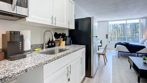 Una cocina moderna con armarios blancos, encimera de granito, cafetera y refrigerador.