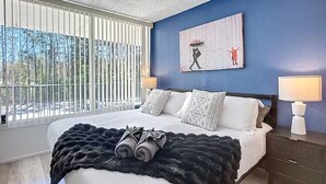 Un dormitorio con una cama grande, dos lámparas de noche, un cuadro en la pared y vistas al exterior.