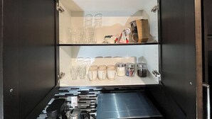 Un armario de almacenamiento con varios estantes que contiene utensilios de cocina, incluyendo tazas, vasos y recipientes.