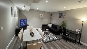 Una sala de estar moderna con comedor, un sofá negro, una mesa de centro y un televisor de pantalla plana.
