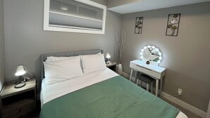 Un dormitorio con cama, mesita de noche, tocador con espejo y decoración en la pared.