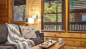 A cozy cabin interior with a wooden interior, a sofa, a coffee table with a tray of snacks, and a window with blinds. - Hidden Cozy Cabin Villa with Hot Tub Close to Everything (Pigeon Forge)
