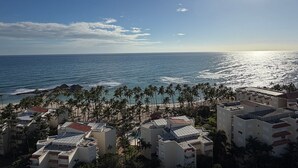 A coastal view with a beach, palm trees, and buildings with flat roofs. - Hemingway By YellowKey (Guayacanes)