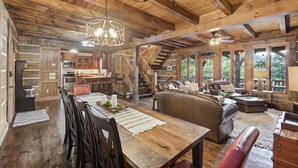En rummelig indretning med træloft, spiseplads med bord og stole, opholdstue med sofaer og et køkkenområde.