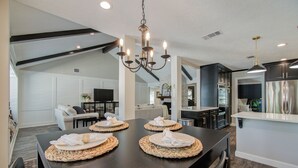 A modern kitchen with a dining area, featuring a dark wooden table with placemats, a chandelier, and built-in appliances. - Chic TX House w/ Pool and Relaxing Atmosphere (Spring)