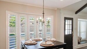 A dining area with a table set for four, a chandelier, and a view through the glass doors. - Chic TX House w/ Pool and Relaxing Atmosphere (Spring)