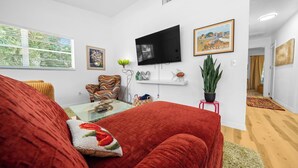 A living room with a red sofa, a television mounted on the wall, and a window with blinds. - The Happy Haven Near Manatee Tours (Crystal River)