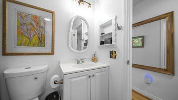 A bathroom with a toilet, sink, mirror, and shelves with towels.