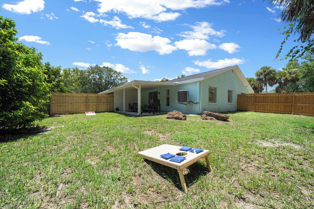 A single-story house with a covered porch, a fenced backyard, and a picnic table with blue napkins.