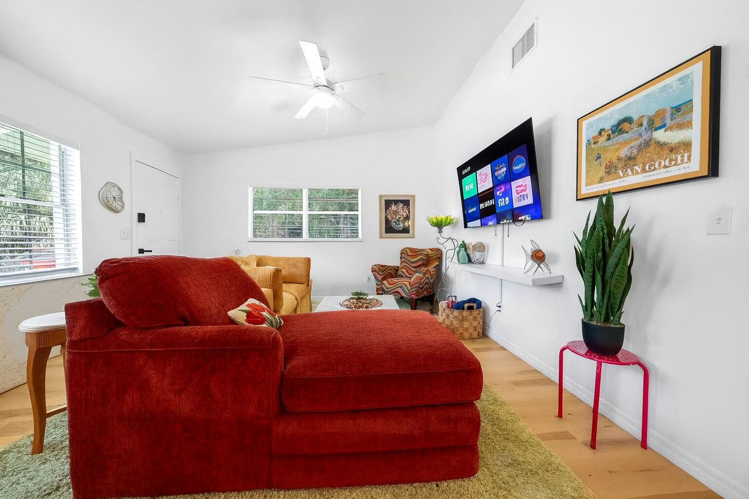 Een moderne woonkamer met een rode bank, een plafondventilator, een flatscreen-tv en een schilderij aan de muur.