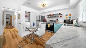 A modern kitchen with white cabinetry, a marble countertop, and a dining area with a glass table and white chairs. - The Happy Haven Near Manatee Tours (Crystal River)