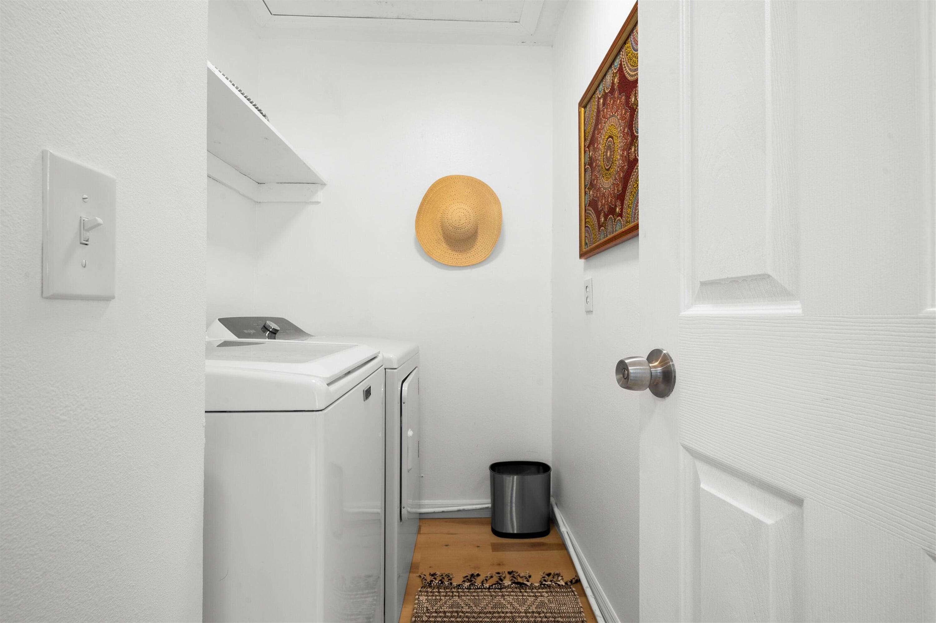 Una sala de lavandería con lavadora, un cesto de basura y una puerta con pomo plateado.