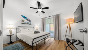 Ein Schlafzimmer mit Bett, Deckenventilator, Nachttischlampen, einem Fernseher und Blick ins Freie.