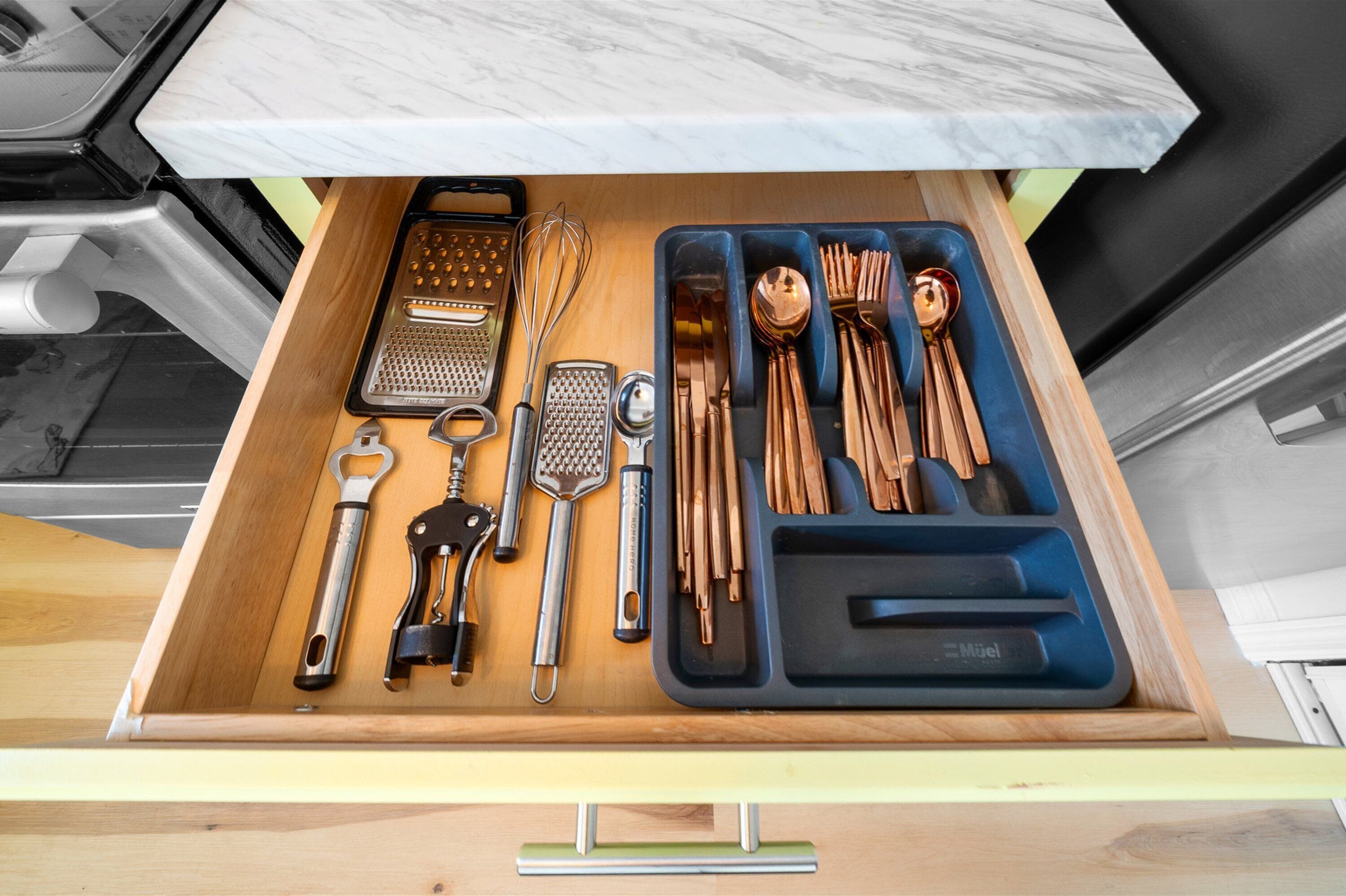 A drawer with kitchen utensils and tools, including a grater, whisk, and various knives.