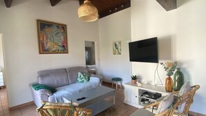 Een woonkamer met een bank, twee rieten fauteuils, een salontafel, een televisie en een klein kastje met een plant.