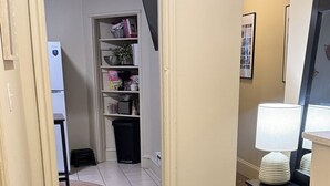 Käytävän lattialla on matto, siellä on musta roskakori, valkoinen jääkaappi ja hylly, jossa on erilaisia esineitä.