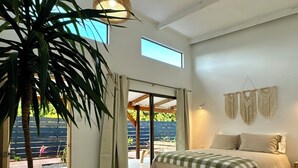 Quarto com cama, uma grande planta em vaso, luz de teto e vista para o exterior.