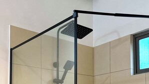 Divisória de chuveiro moderna com chuveiro manual, chuveiro de chuva e escova manual. Há dois frascos de shampoo e condicionador numa prateleira.