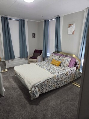 A bedroom with a bed, a chair, a window with curtains, and a wall with a poster. - Cozy 1-bedroom house in lovely Springfield with AC (Springfield)