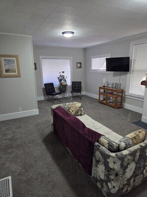 A living room with a sofa, chairs, a TV, and a window with blinds. - Cozy 1-bedroom house in lovely Springfield with AC (Springfield)