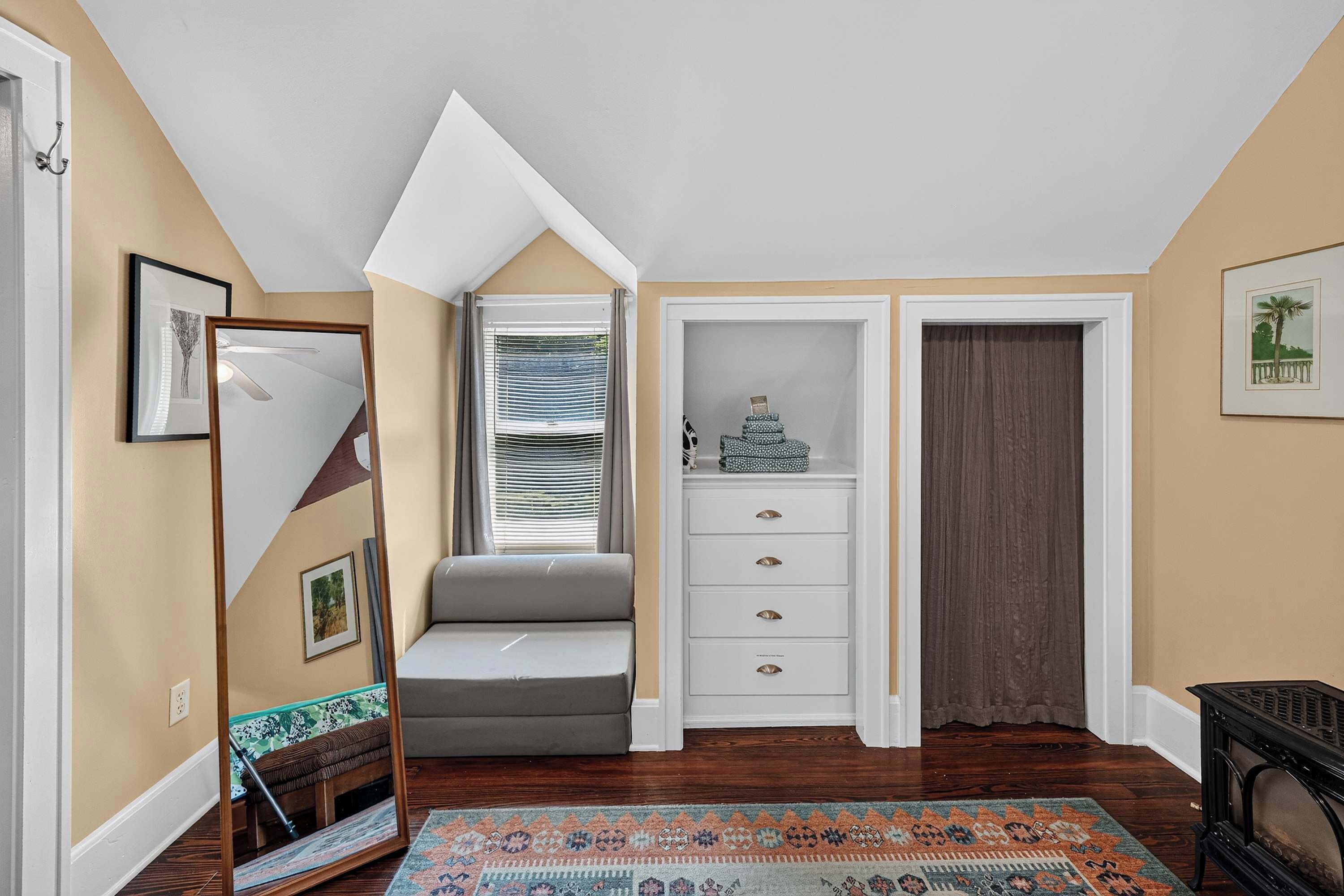 A room with a sloped ceiling, a bench, a white cabinet with drawers, a patterned rug, and a framed picture on the wall.