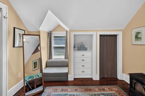 A room with a sloped ceiling, a bench, a white cabinet with drawers, a patterned rug, and a framed picture on the wall. - Historic Studebaker Carriage House- Upper Level (South Bend)