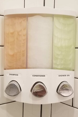 A wall-mounted dispenser with three compartments labeled for shampoo, conditioner, and shower gel. - Historic South Bend Home: Art, Comfort & Charm (South Bend)