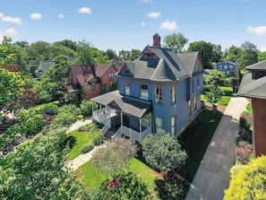 A two-story house with a porch, surrounded by well-maintained gardens and a clear sky. - Historic South Bend Home: Art, Comfort & Charm (South Bend)