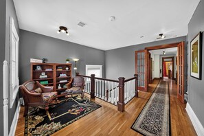 Un hall d’entrée spacieux avec un escalier en bois, un coin salon avec un canapé et des étagères, et un tapis décoratif.