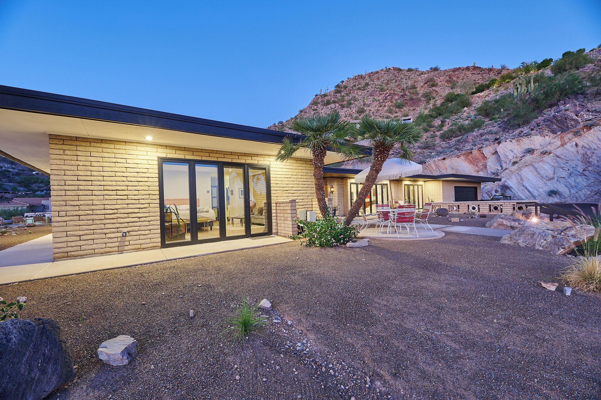 A modern house with a brick exterior, large glass windows, and a patio area with outdoor furniture.