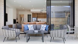 Una sala de estar moderna con un sofá, dos sillones y una mesa de centro. Hay un ventanal corredero que da a un balcón con mobiliario exterior.