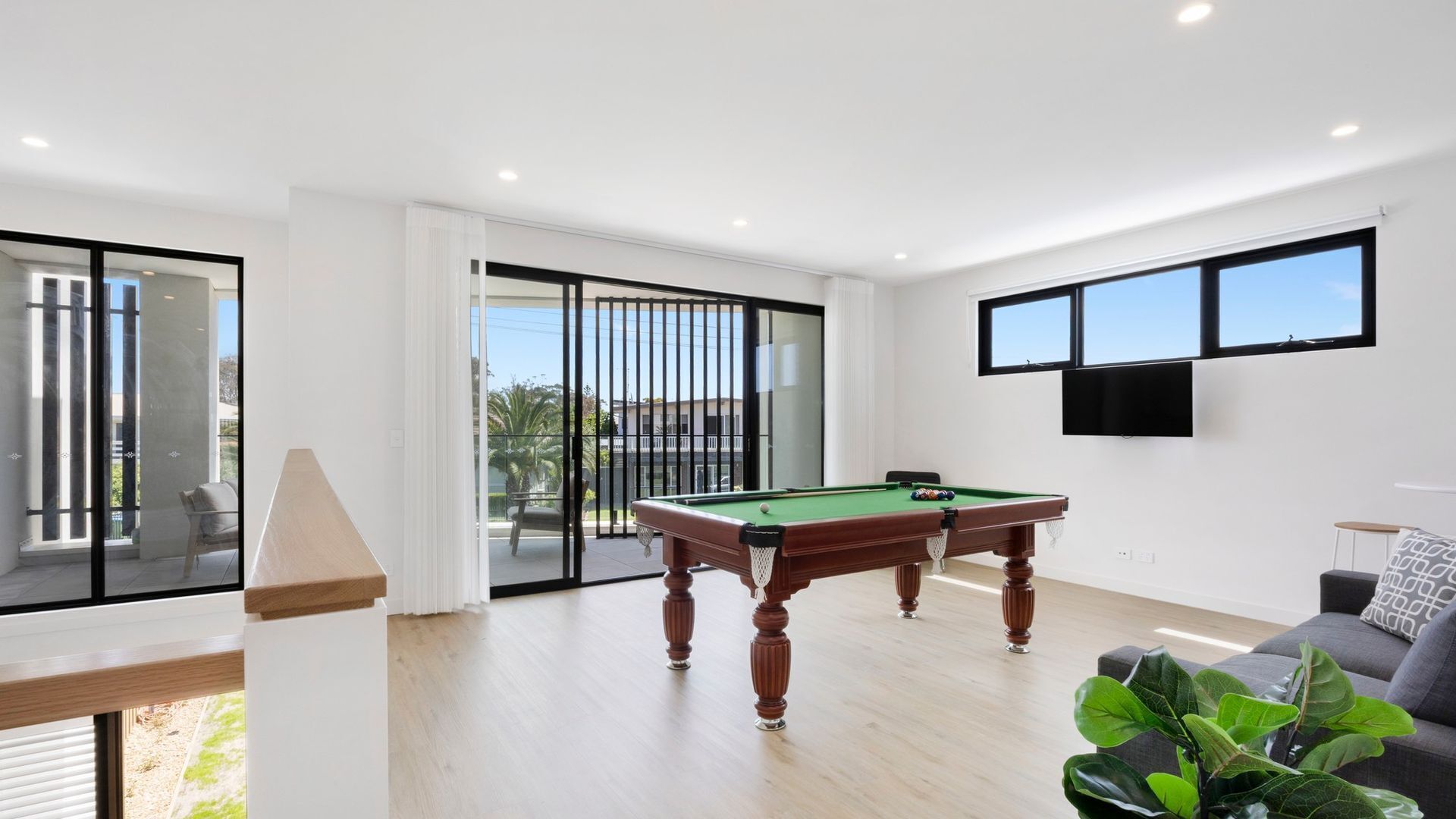 A modern living room with a pool table, large windows, and a flat-screen TV.