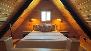 A cozy attic bedroom with a wooden sloped ceiling, a central bed with pillows, and two bedside lamps. - Charming 1 BR Cabin at Persimmon & Pine Hollow- Secluded Feel, Close to Town (Dublin)