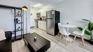 A modern kitchen with white cabinets, a stainless steel refrigerator, and a microwave. There is a dining area with a round table and two white chairs. - 5-202 Breakwater (Jacksonville)