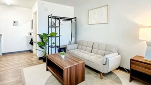 A modern living room with a beige sofa, a wooden coffee table, a black metal shelf unit, and a small plant. - 5-202 Breakwater (Jacksonville)