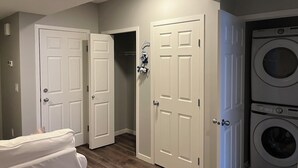 A laundry room with a Samsung washer and dryer, two white doors, and a white couch. - Modern 1BD Suite•5 star Comfort•Beaumont•Edmonton (Beaumont)