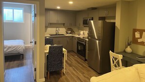 A compact kitchen with modern appliances, a dining area with a patterned chair, and a small seating area with a white chair. - Modern 1BD Suite•5 star Comfort•Beaumont•Edmonton (Beaumont)