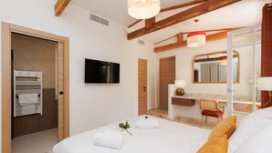 Una habitación de hotel moderna con una cama grande, televisión, baño con espejo y techo de madera.