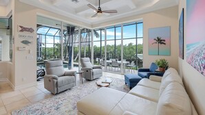 A spacious living area with a large window, a ceiling fan, and a view of the outdoors. - Tigertail Family Beach Home - Completely Remodeled, Ocean Views, Walk to Beach! (Marco Island)