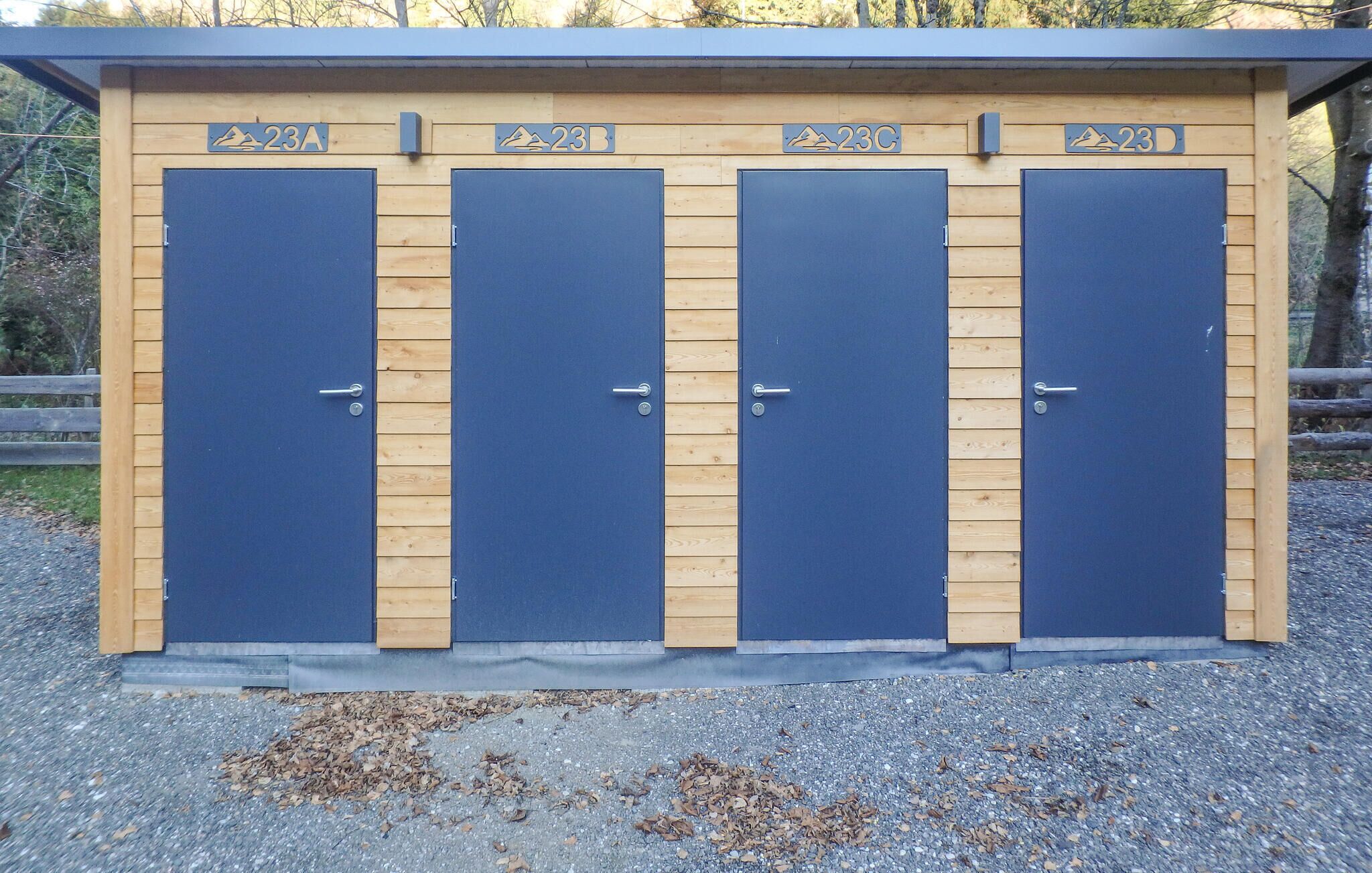 A row of four blue doors with wooden paneling, each marked with a number (23A, 23B, 23C, 23D) and a mountain icon, indicating a row of changing rooms or facilities.