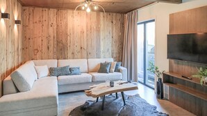 Ein modernes Wohnzimmer mit einem Ecksofa, einer Wandpaneele aus Holz, einem Wand-Fernseher und einem großen Fenster.