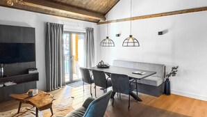 Un salon moderne avec un coin repas, des poutres apparentes en bois au plafond et des luminaires suspendus.