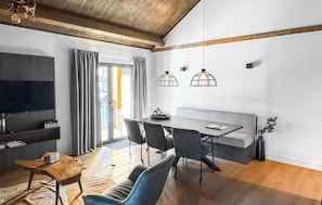 Ein modernes Wohnzimmer mit Essbereich, Holzbalkendecke und Pendelleuchten.