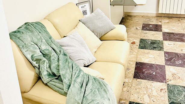 Une pièce avec un canapé beige, une couverture verte et un sol à carreaux.