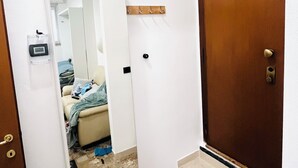 Un couloir étroit avec une porte en bois, un miroir et une petite étagère avec des crochets.