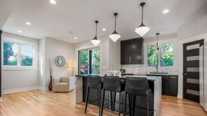 A modern kitchen with a central island, bar stools, pendant lighting, and large windows. - Private Ultra Modern Mansion - Country Club Plaza (Kansas City)