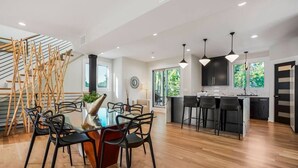 A modern kitchen with a central island, black bar stools, and a dining area with a glass table and chairs. - Private Ultra Modern Mansion - Country Club Plaza (Kansas City)